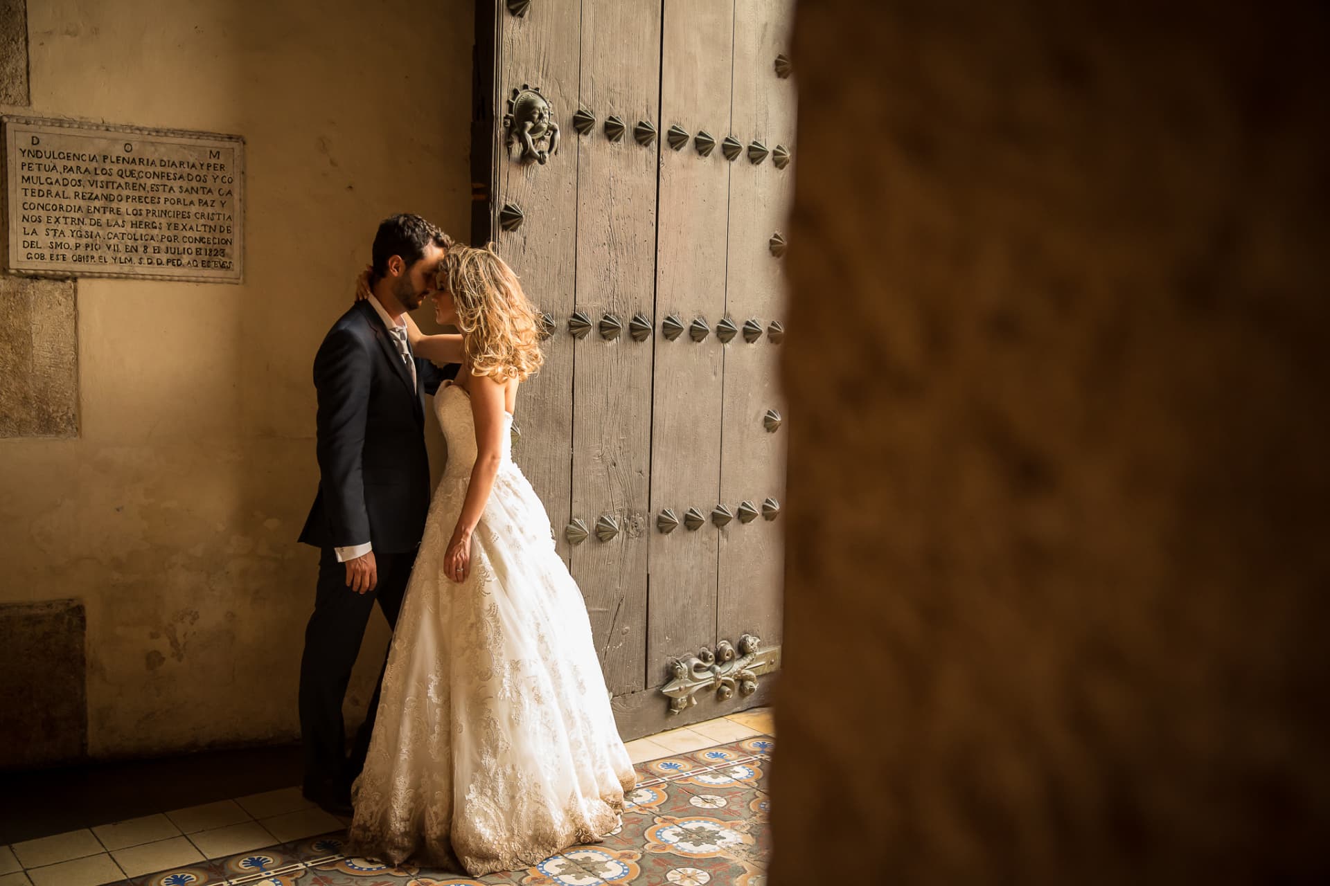 Novios compartiendo un momento íntimo junto a una puerta histórica iluminada