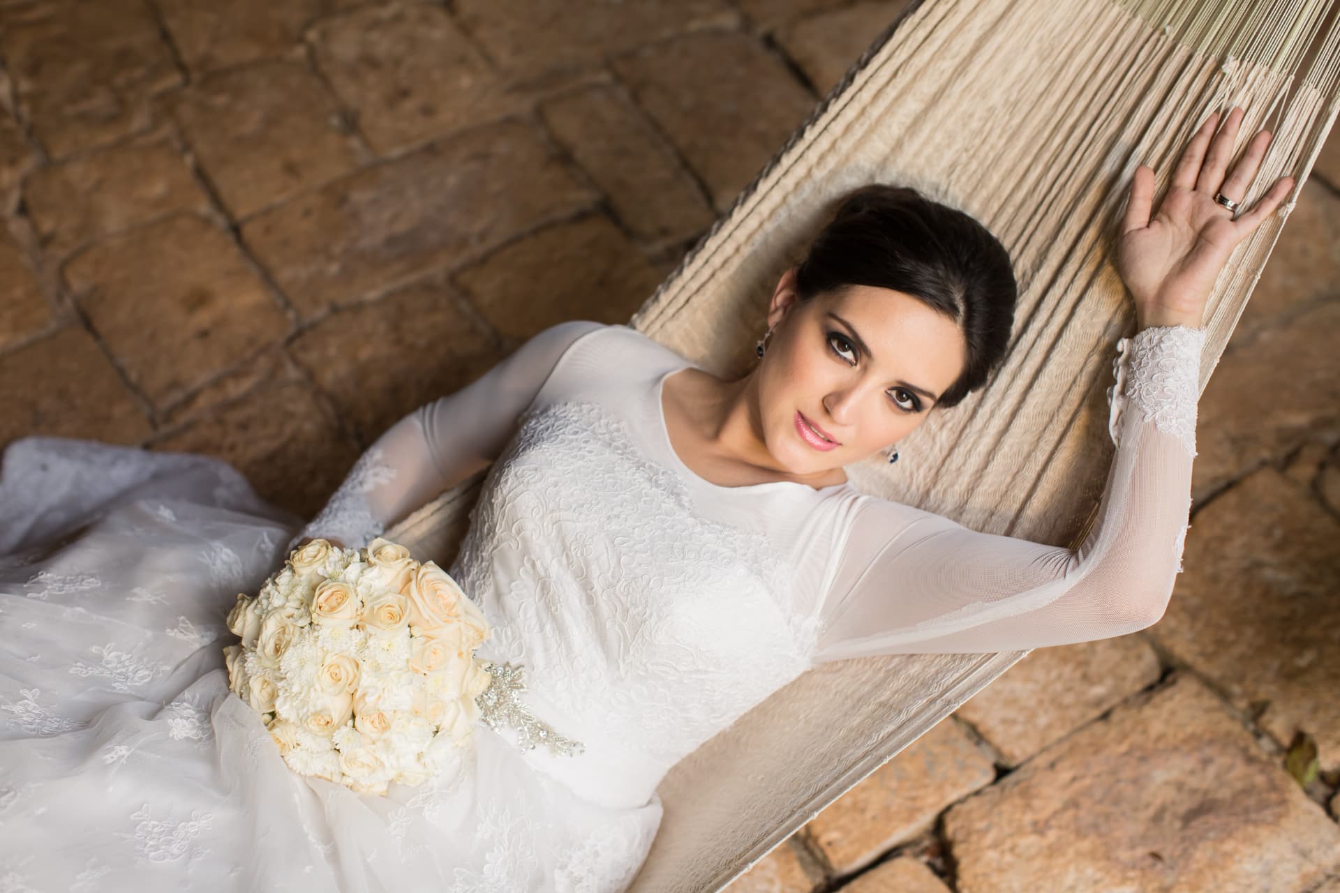 Retrato editorial de novia recostada en una hamaca con ramo de rosas blancas