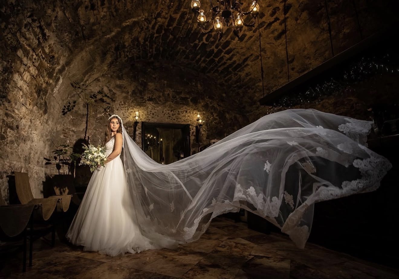 Novia con velo largo flotando en un salón de piedra iluminado