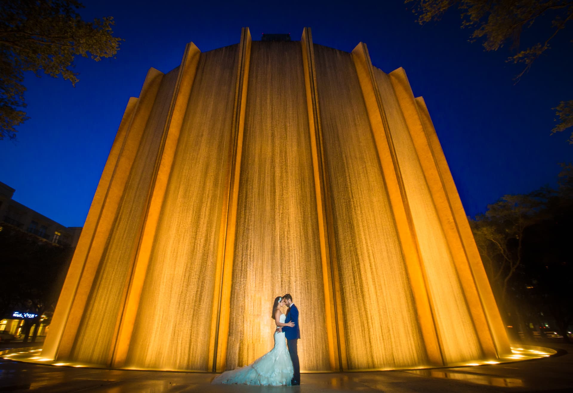 Novios besándose frente a una fuente monumental iluminada por la noche