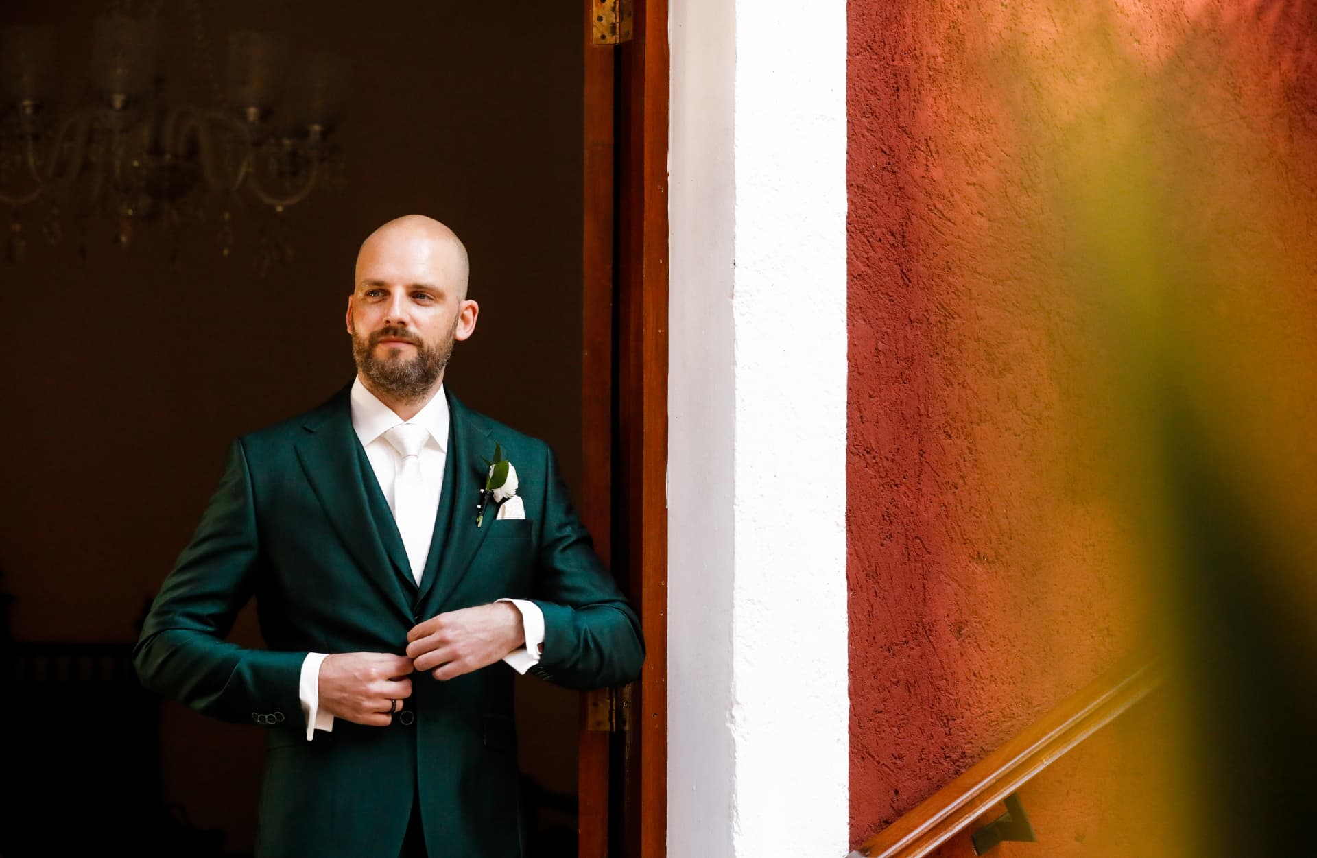 Retrato editorial del novio ajustando su traje verde durante los preparativos