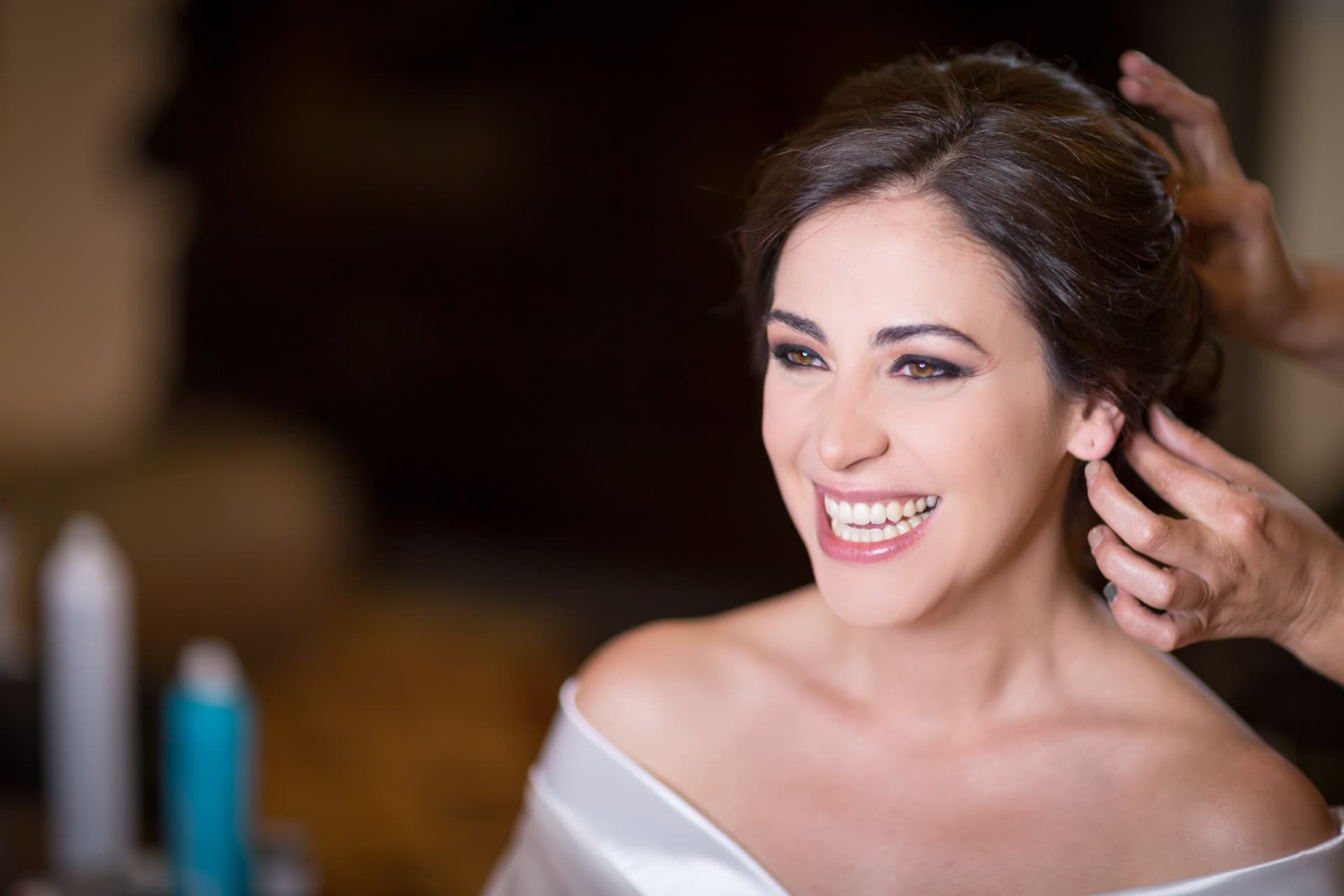 Novia sonriendo mientras terminan de arreglar su cabello durante los preparativos