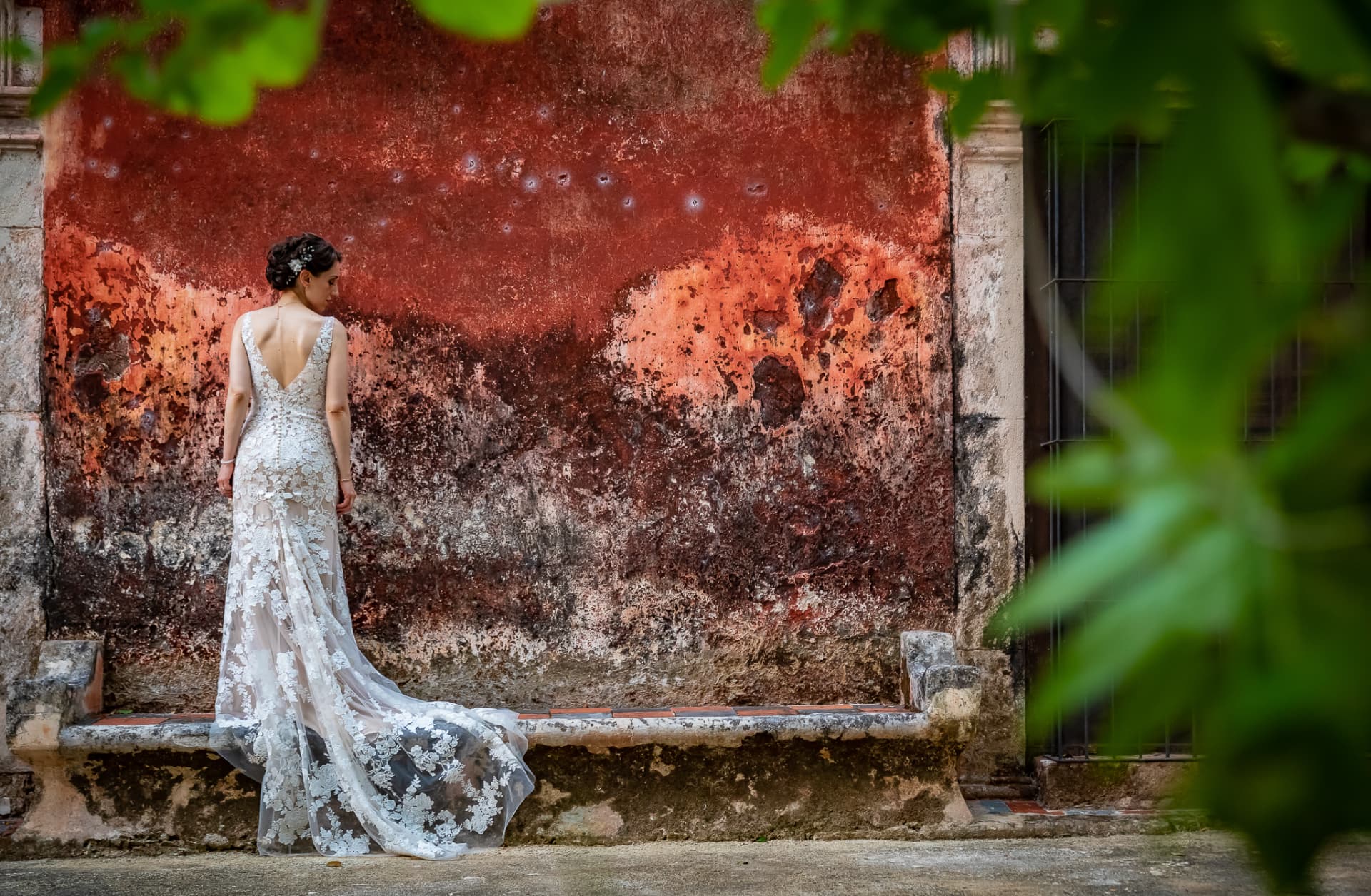 Novia con vestido de encaje frente a un muro colonial de textura rojiza