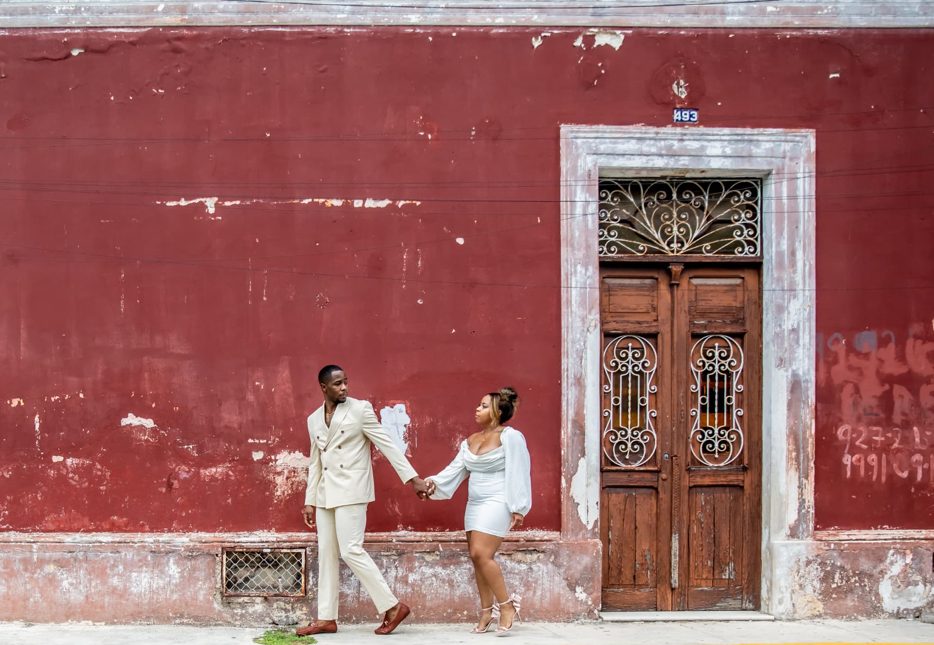 Pareja caminando de la mano frente a un muro colonial rojo, sesión save the date